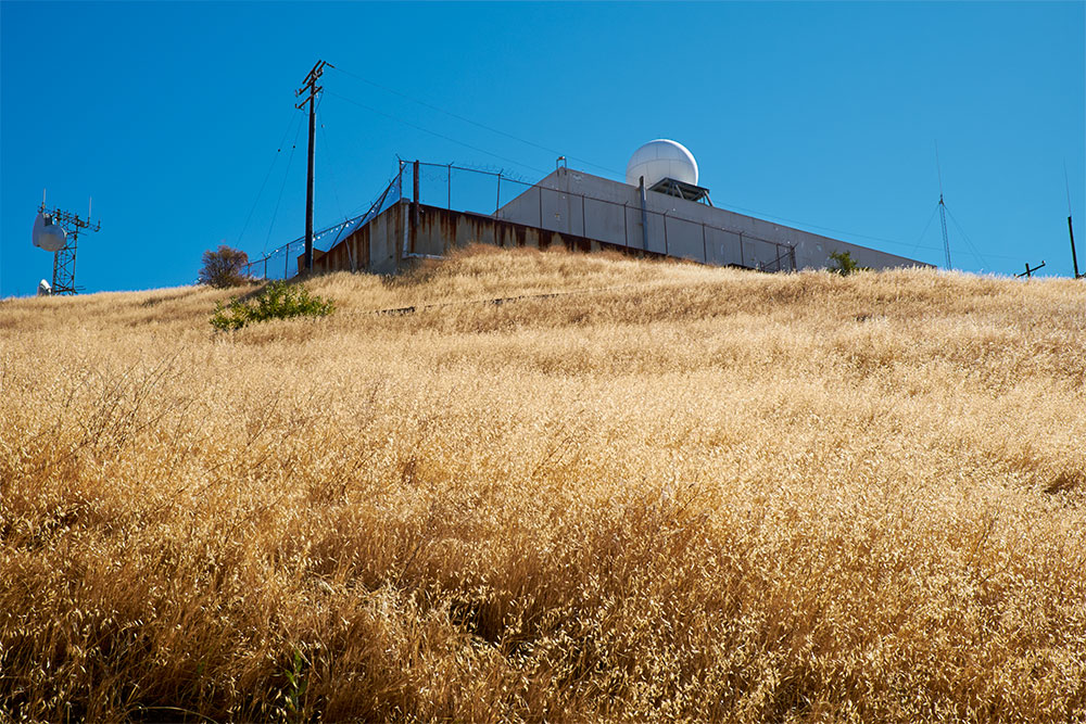 A field of dry grasses with a fenced off radar dome in the background
