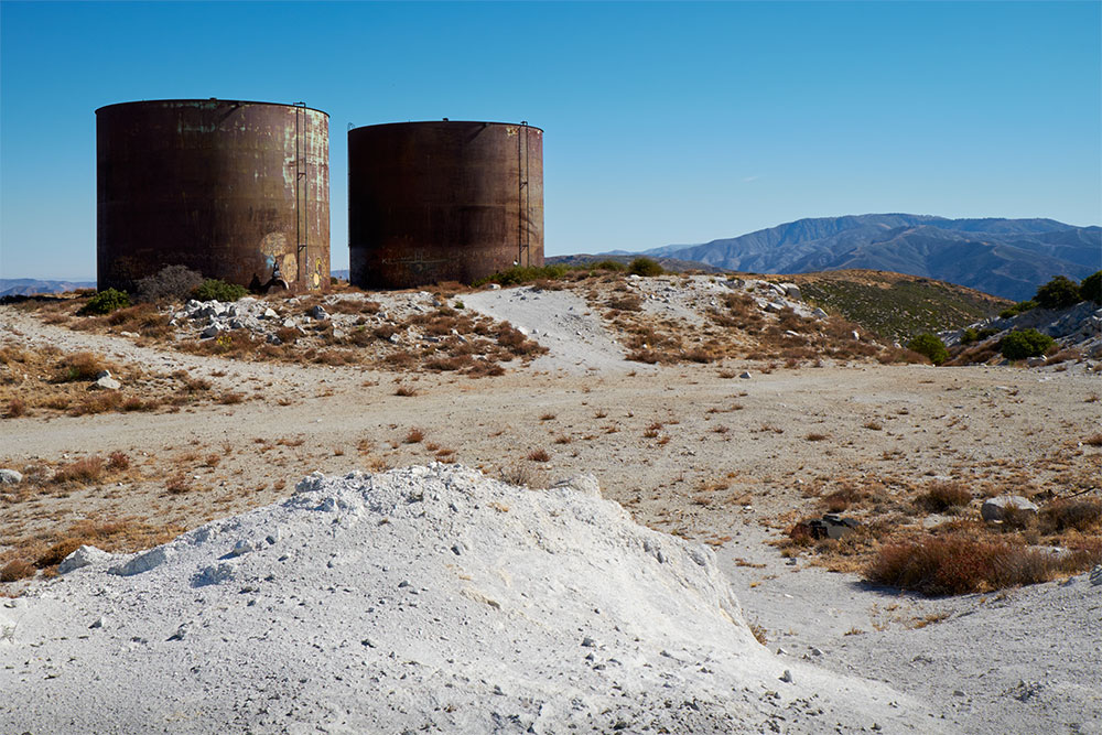 Two large metal tanks and a dirt road with small brush