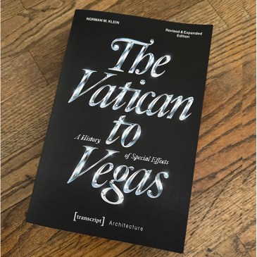 A book titled "The Vatican to Vegas" on a textured wood floor